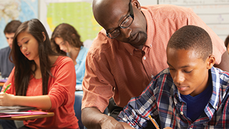 A teacher helping a student while the other students continue to work on their worksheet