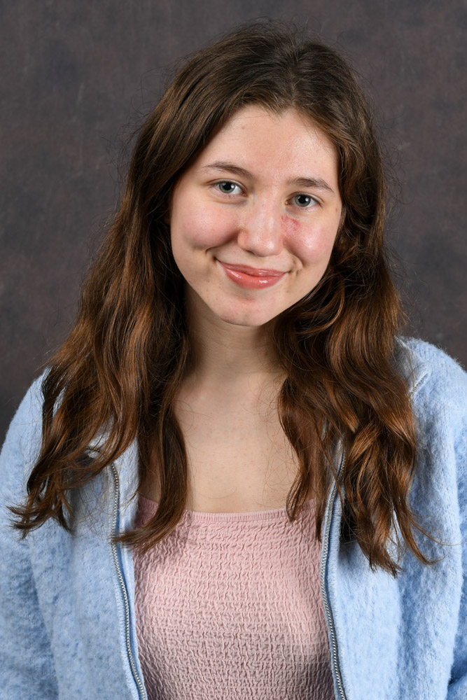 A person poses and smiles for a photo with a professional background behind her.