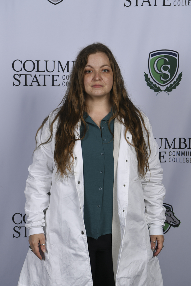 A woman stands in front of a white background.