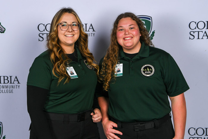 Two women stand in front of a white background.