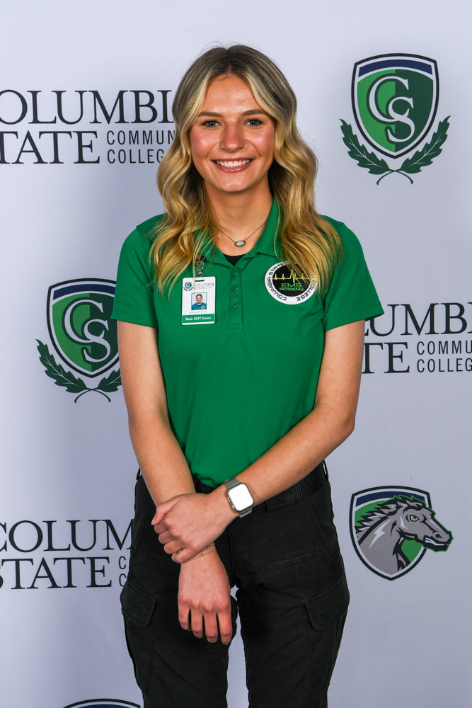A woman stands in front of a white background.