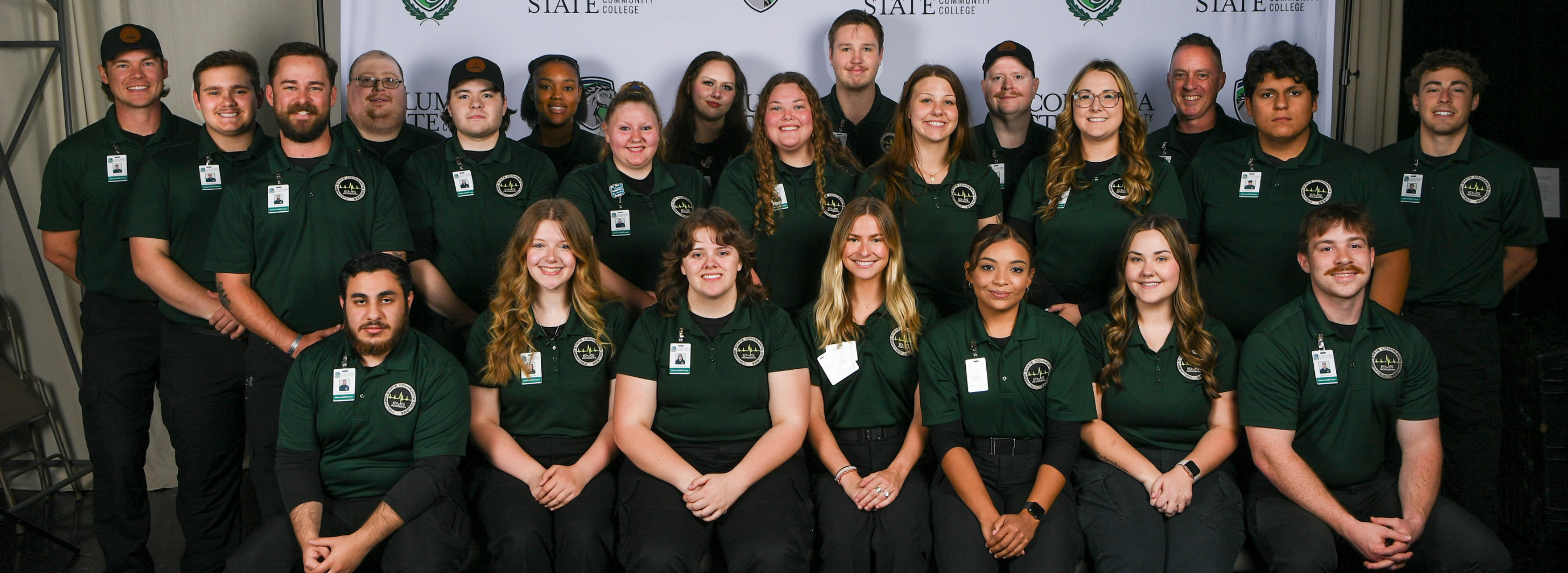 A group of people wearing dark green collar shirts sit and stand for a photo.